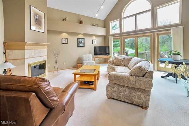 living area featuring carpet flooring, high vaulted ceiling, a tiled fireplace, and baseboards