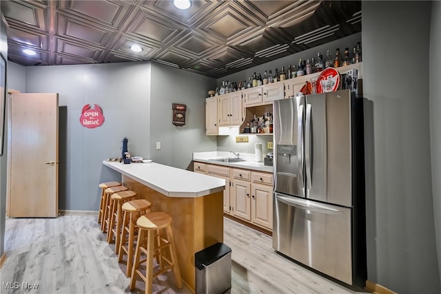 kitchen featuring stainless steel refrigerator with ice dispenser, light wood-type flooring, light countertops, a sink, and an ornate ceiling