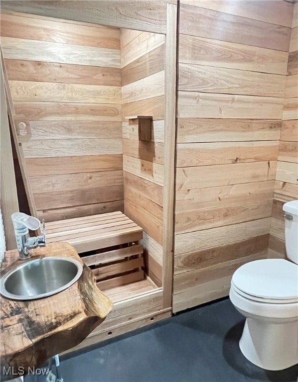 bathroom with concrete flooring, wood walls, and toilet