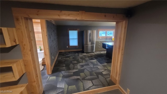 corridor with a sink, dark colored carpet, and baseboards