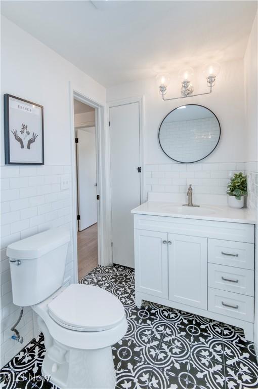 bathroom with tile patterned floors, wainscoting, vanity, tile walls, and toilet