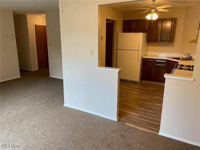 kitchen with light countertops, a ceiling fan, a sink, freestanding refrigerator, and baseboards