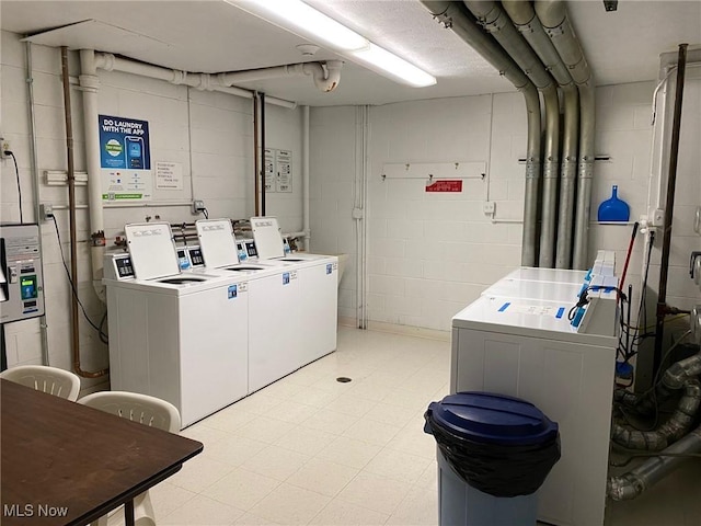 common laundry area with concrete block wall, washer and dryer, and light floors