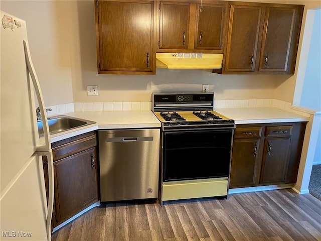 kitchen with stainless steel dishwasher, range with gas stovetop, under cabinet range hood, dark wood-type flooring, and freestanding refrigerator