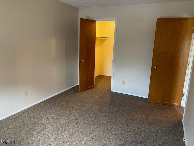 unfurnished bedroom featuring a closet, dark colored carpet, a spacious closet, and baseboards