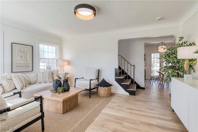 living area featuring light wood-type flooring, arched walkways, a wealth of natural light, and stairs