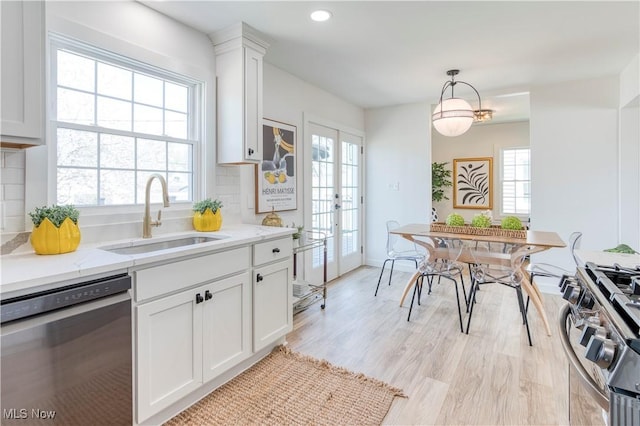 kitchen with white cabinets, stainless steel appliances, a sink, decorative backsplash, and decorative light fixtures
