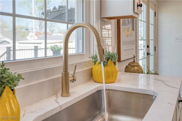 room details with white cabinets, light stone counters, and a sink