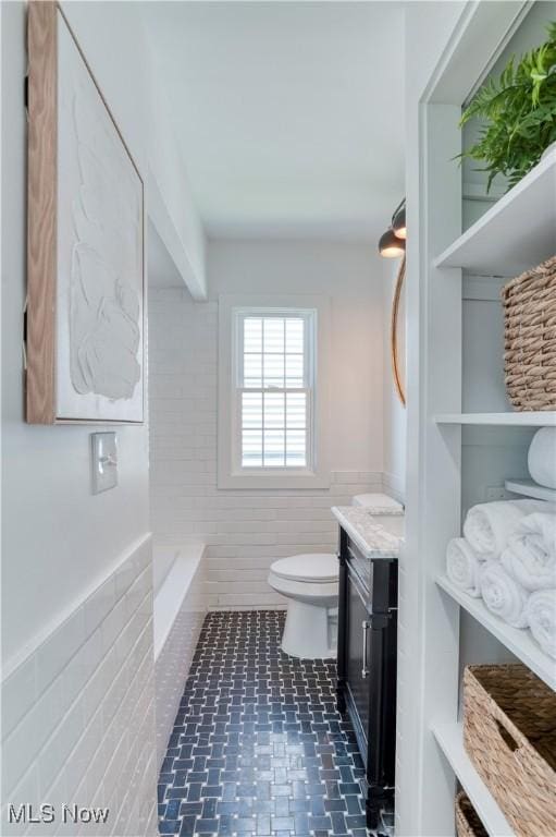 full bathroom featuring wainscoting, vanity, a bathtub, tile walls, and toilet