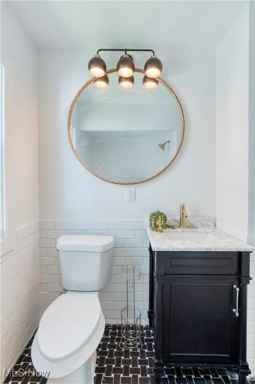 bathroom featuring tile walls, toilet, vanity, and a wainscoted wall