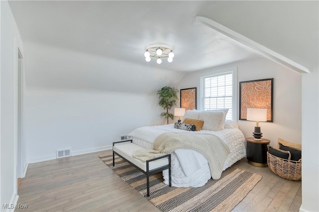 bedroom with lofted ceiling, wood finished floors, visible vents, and baseboards