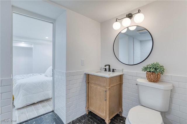 bathroom featuring tile walls, toilet, ensuite bathroom, and wainscoting