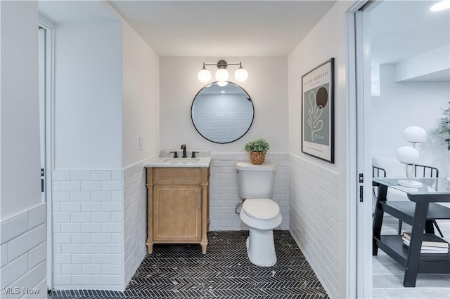 bathroom featuring tile patterned floors, toilet, vanity, tile walls, and wainscoting