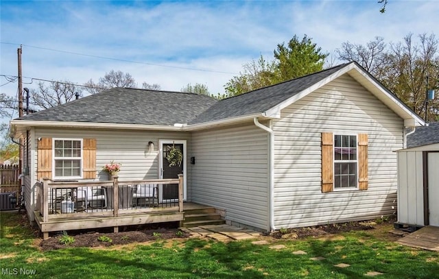 back of house featuring a shingled roof, a storage shed, a yard, a wooden deck, and an outbuilding