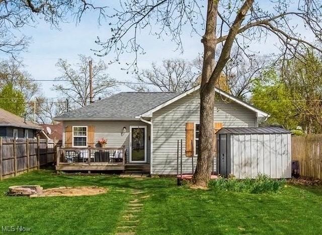 back of house with a fenced backyard, a yard, a deck, and a storage unit