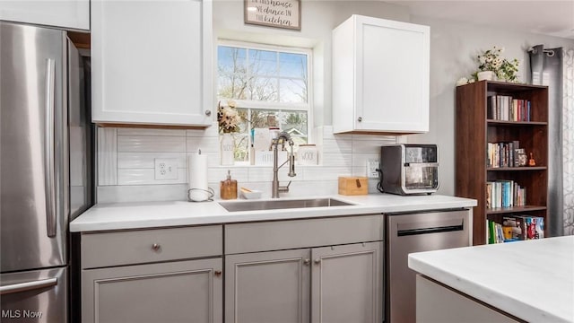 kitchen with white cabinets, a sink, tasteful backsplash, light countertops, and appliances with stainless steel finishes