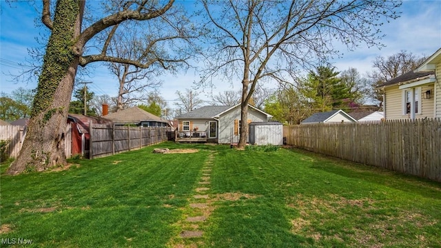 view of yard with a wooden deck, a fenced backyard, an outdoor structure, and a shed