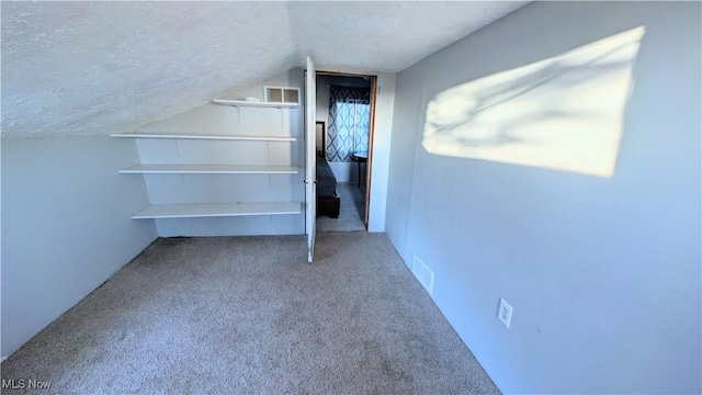 interior space with visible vents, vaulted ceiling, carpet flooring, and a textured ceiling