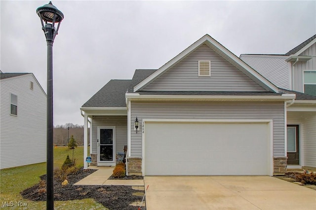 view of front facade featuring concrete driveway, stone siding, a shingled roof, and a garage