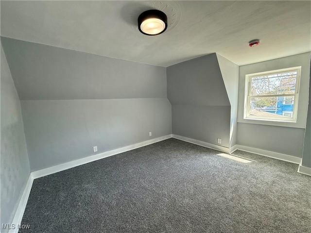 additional living space featuring dark colored carpet, vaulted ceiling, and baseboards