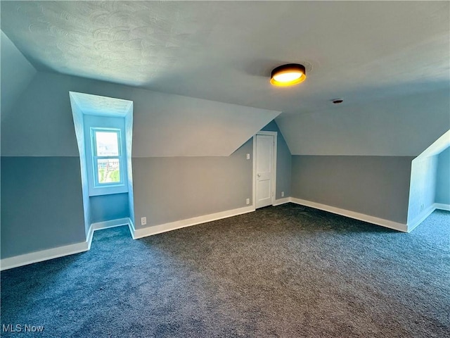 bonus room featuring dark carpet, vaulted ceiling, and baseboards