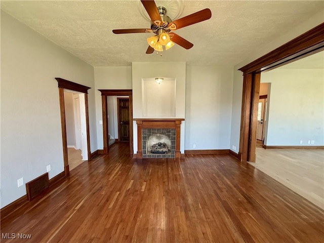 unfurnished living room with a ceiling fan, a textured ceiling, hardwood / wood-style flooring, a tiled fireplace, and visible vents