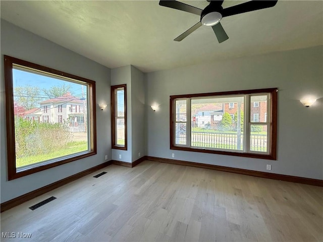 empty room with light wood-type flooring, visible vents, baseboards, and ceiling fan