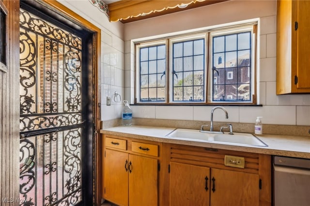 kitchen featuring brown cabinetry, stainless steel dishwasher, light countertops, and a sink