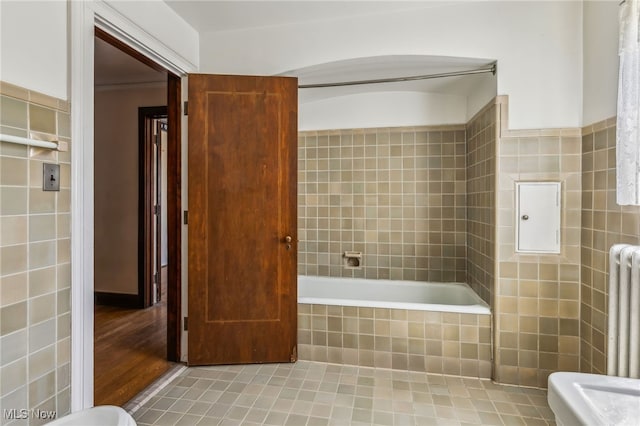 full bathroom featuring radiator heating unit, a tile shower, tile walls, and a relaxing tiled tub
