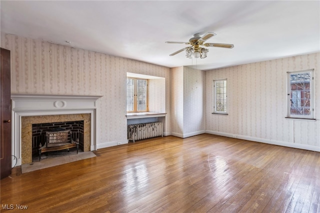 unfurnished living room featuring radiator, wallpapered walls, wood-type flooring, and a ceiling fan