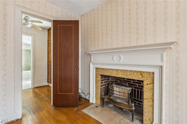 interior details featuring a fireplace with flush hearth, baseboards, wallpapered walls, wood finished floors, and ceiling fan