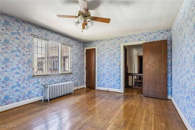 spare room with wood-type flooring, baseboards, ceiling fan, and radiator