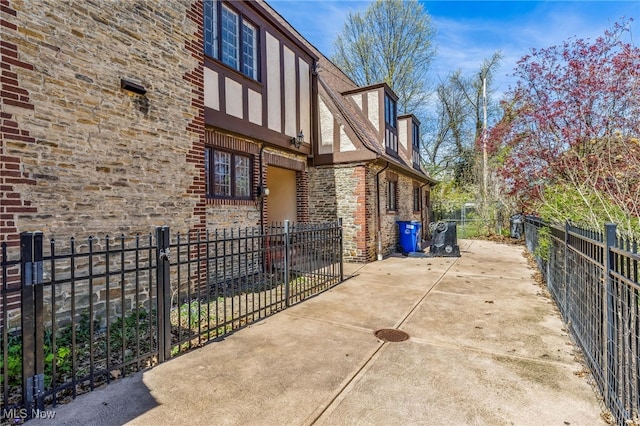 view of side of property featuring a patio area, stone siding, and a fenced backyard