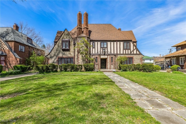 tudor-style house featuring brick siding, a chimney, and a front lawn