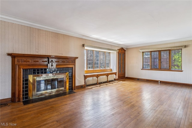 unfurnished living room featuring hardwood / wood-style floors, a tile fireplace, ornamental molding, and radiator