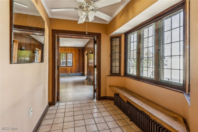 corridor featuring radiator, wood walls, light carpet, crown molding, and baseboards
