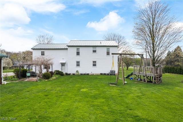 rear view of house featuring a lawn, central AC, a playground, and metal roof