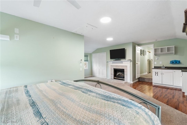 bedroom with lofted ceiling, baseboards, a brick fireplace, and dark wood-style flooring