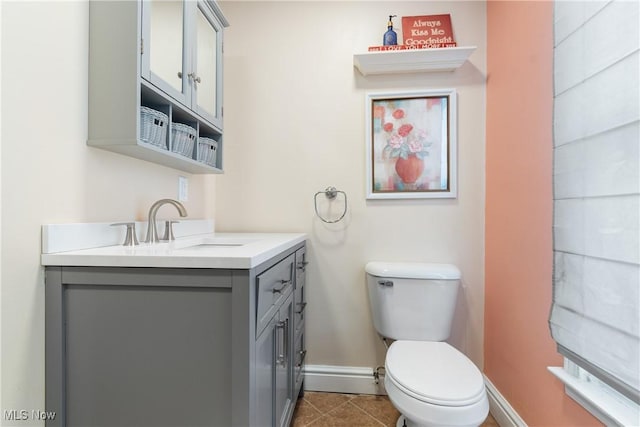 half bath with baseboards, tile patterned flooring, vanity, and toilet