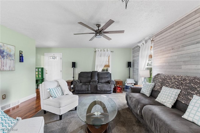 living room featuring ceiling fan, wood finished floors, visible vents, and a textured ceiling