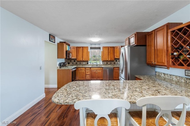 kitchen featuring a sink, brown cabinetry, baseboards, a peninsula, and appliances with stainless steel finishes