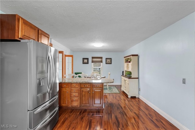 kitchen with a textured ceiling, brown cabinetry, stainless steel fridge with ice dispenser, a peninsula, and dark wood-style flooring