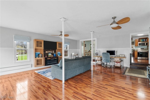 living area featuring a baseboard radiator, a ceiling fan, a wainscoted wall, and wood finished floors