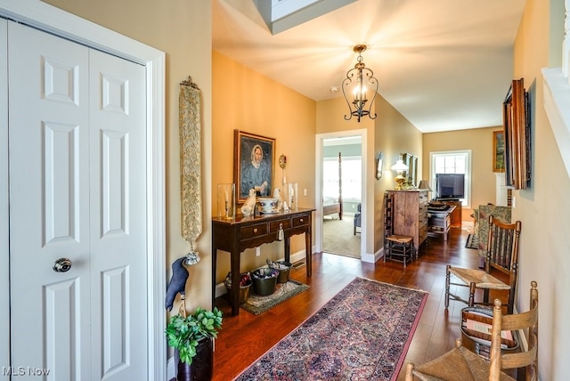 foyer featuring baseboards, dark wood-style floors, and a notable chandelier