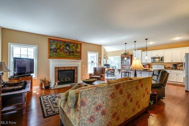 living area featuring recessed lighting, a brick fireplace, a wealth of natural light, and dark wood-style flooring