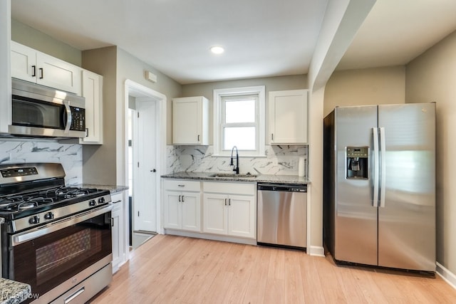 kitchen with a sink, white cabinets, stainless steel appliances, backsplash, and light stone countertops