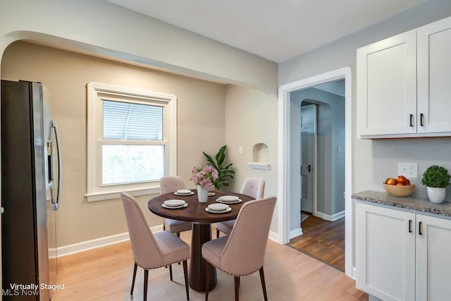 dining space featuring baseboards, arched walkways, and light wood-style floors