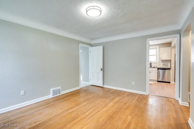 empty room with baseboards, a textured ceiling, visible vents, and light wood-type flooring