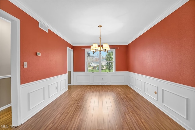 unfurnished dining area with a chandelier, wood finished floors, visible vents, and a wainscoted wall