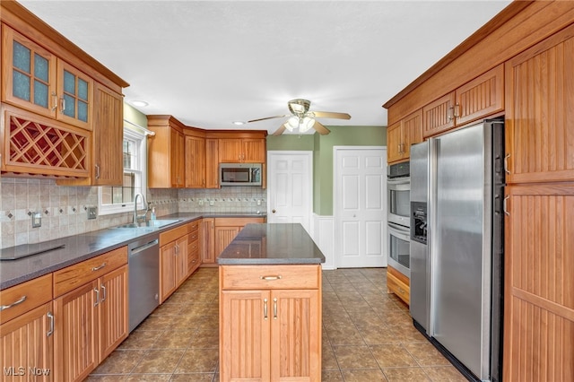 kitchen with stainless steel appliances, a ceiling fan, a sink, a kitchen island, and tasteful backsplash
